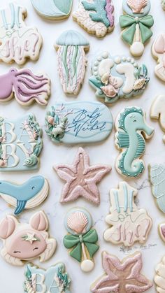 many decorated cookies on a table with writing and seashells in blue, green, pink and white