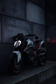 a white and black motorcycle parked in front of a concrete wall with red lights on it