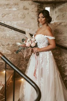 a woman in a wedding dress is standing on the stairs with her bouquet and looking at the camera