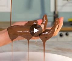 a person holding chocolate dripping from their hands over a bowl full of melted chocolate on the counter