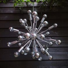 a chandelier made out of metal balls hanging from a wooden wall next to a potted plant