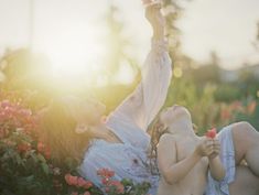 two women laying on the ground in front of some flowers and one is holding a flower