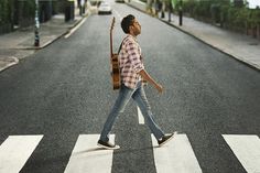 a man walking across a street holding a guitar