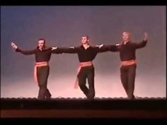 three men in black and red outfits are dancing on a stage with their arms outstretched