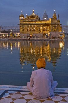 a man sitting on the edge of a body of water with a building in the background