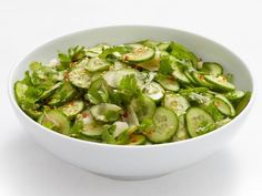 a white bowl filled with cucumbers and other green vegetables on top of a table