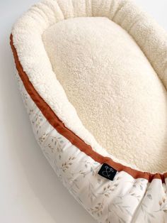 a white dog bed with brown trim on the bottom and sides, sitting on a white surface