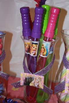 there are many different colored pens in the glass vases on the table with candy and candies