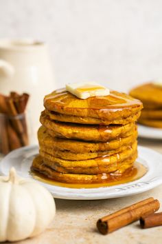 a stack of pancakes on a plate with syrup and cinnamon sticks next to the plates