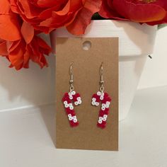 a pair of red and white cross earrings sitting on top of a card next to flowers