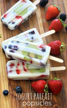 popsicles with fruit and yogurt are on a wooden table next to strawberries