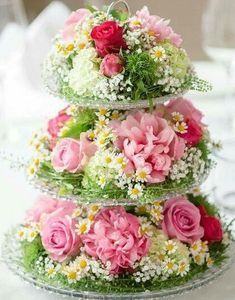 three tiered cake with pink and white flowers on the top, sitting on a table