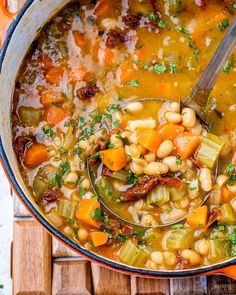 a pot filled with soup and vegetables on top of a wooden table next to a spoon