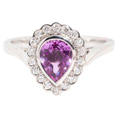 Sweetly crafted in 18 carat white gold, The Priya Ring is a delight. Her pear shaped pink purple sapphire is set in a halo of diamond embellished lace. A loving way to ask to share a life with your beloved, she is the perfect mix of romance and glamour. The Priya Ring Gem Details  The centre pear shaped purplish pink sapphire measures 7.20x5.50x3.85 millimetres and is estimated to weigh 1.10 carats. The sapphire is lightly included and shows very slight signs of wear. The eighteen round brillian Pinkish Purple, Purple Rings, Purple Sapphire, Sapphire Diamond Ring, Sapphire Diamond, Jewelry Rings Engagement, Vintage Jewellery, Round Brilliant Cut Diamond, Pink Sapphire