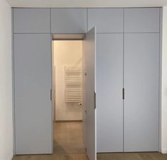 an empty room with white closets and wood flooring in the center is a radiator on the wall