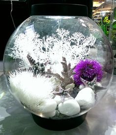 a fish bowl filled with white rocks and purple flowers on top of a glass table