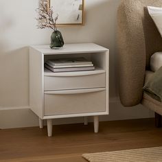 a white nightstand with two drawers next to a bed and a painting on the wall