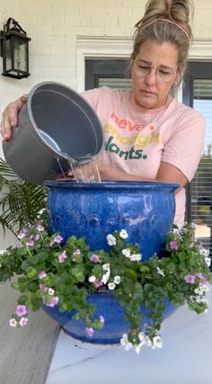 a woman is pouring water into a blue pot with flowers in front of her on a table