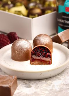 two desserts on a white plate with raspberries and chocolate in the background