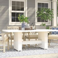 a white table and chairs sitting on top of a patio next to a house with windows