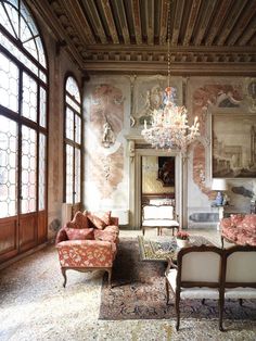 a living room with couches, chairs and chandelier in front of large windows