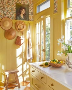 a kitchen with yellow walls and white counter tops, decorated with hats hanging on the wall