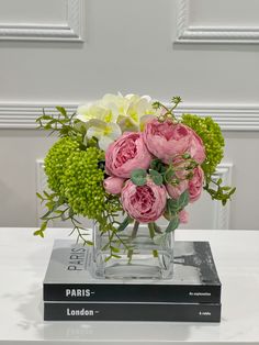 pink and white flowers are in a clear vase on top of a book that is sitting on a table