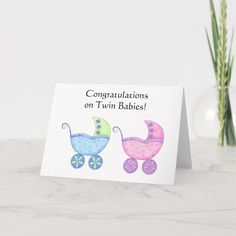 congratulations on twin babies card with pink and blue stroller in the center, next to a vase filled with flowers