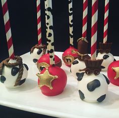 chocolate covered apples with decorations on them sitting on a white plate next to red and black candles