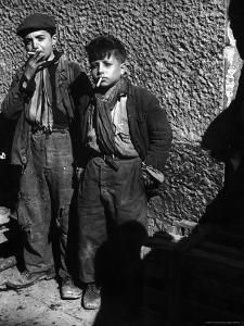 two men standing next to each other in front of a building with a brick wall