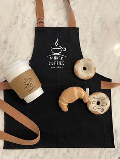 coffee and donuts are sitting on the counter next to a black apron that says finn's coffee