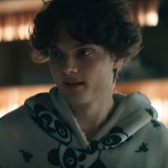 a young man with curly hair wearing a hoodie and looking off to the side