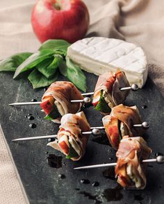 several appetizers with meat and cheese on skewers next to an apple