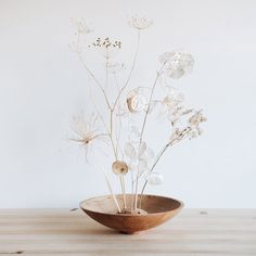 a wooden bowl filled with flowers on top of a table next to a white wall