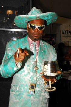 a man in a green suit and hat holding a silver cup with gold chains on it