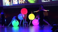 some people are performing on stage with colorful balls in the air and lights behind them