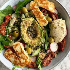 a white bowl filled with salad topped with meat and veggies on top of a marble table