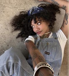 a woman with tattoos on her arms and legs laying down next to a cement wall