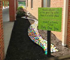 a sign that is on the side of a building with rocks and grass around it