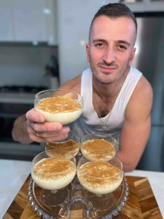 a man is holding four desserts in front of him on a wooden platter