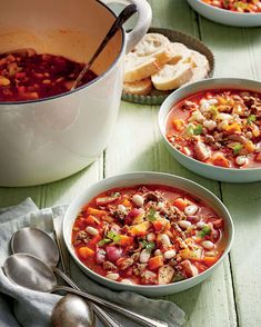 three bowls of soup on a table with bread and spoons next to it,