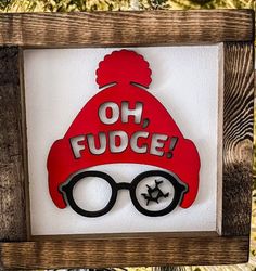 a red hat and glasses with the words oh fudge on it is mounted in a wooden frame