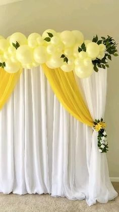 a white curtain with yellow drapes and flowers on the top is decorated with balloons