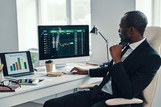 a man in a suit sitting at a desk with a computer and monitor on it