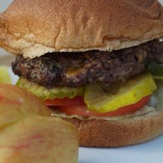 a hamburger and an apple on a white plate with some sort of fruit in the background