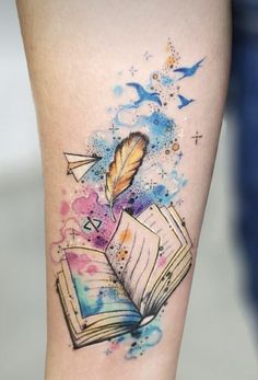 a tattoo with an open book and a feather on the inside of it, surrounded by watercolor splashes