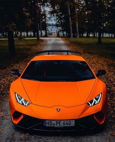 an orange sports car parked on the side of a road in front of some trees