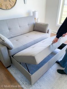 a man standing in front of a couch with a pull out bed underneath it and a clock on the wall