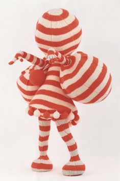 a red and white knitted doll wearing a striped dress, holding a large ball