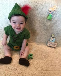 a baby sitting on the floor wearing a green outfit